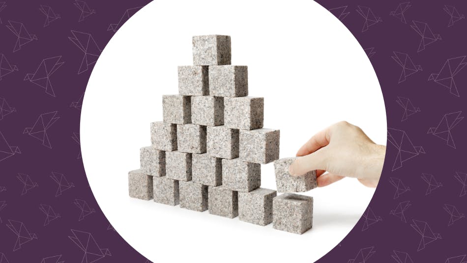 Unstable. Hand removing one block of a pyramid made of small granite rock blocks.