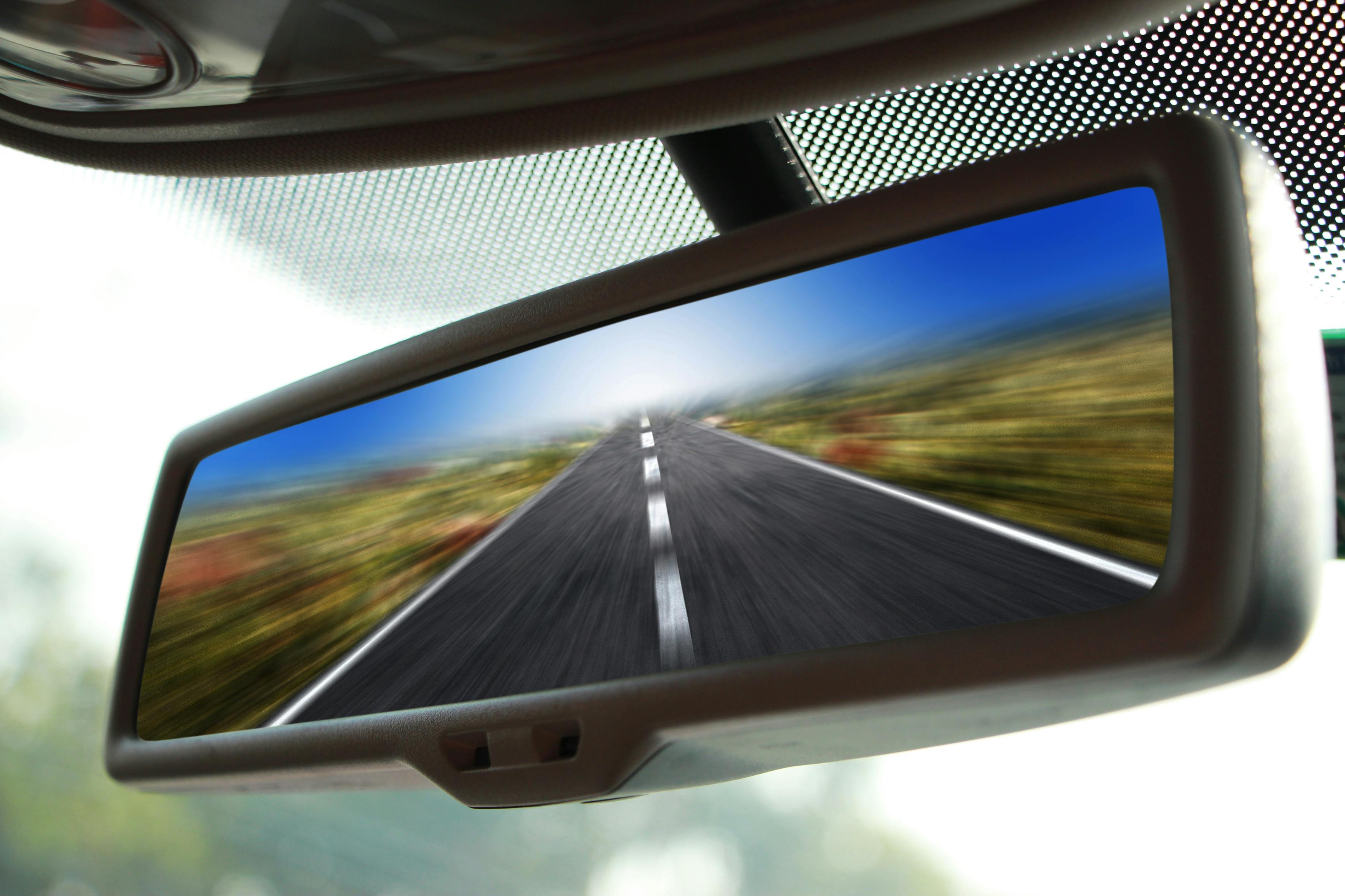 A closeup of a rearview mirror on a car driving fast on a road.