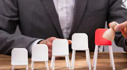 Close-up Of Businessperson`s Finger Placing Pawn On Red Chair Over Wooden Desk