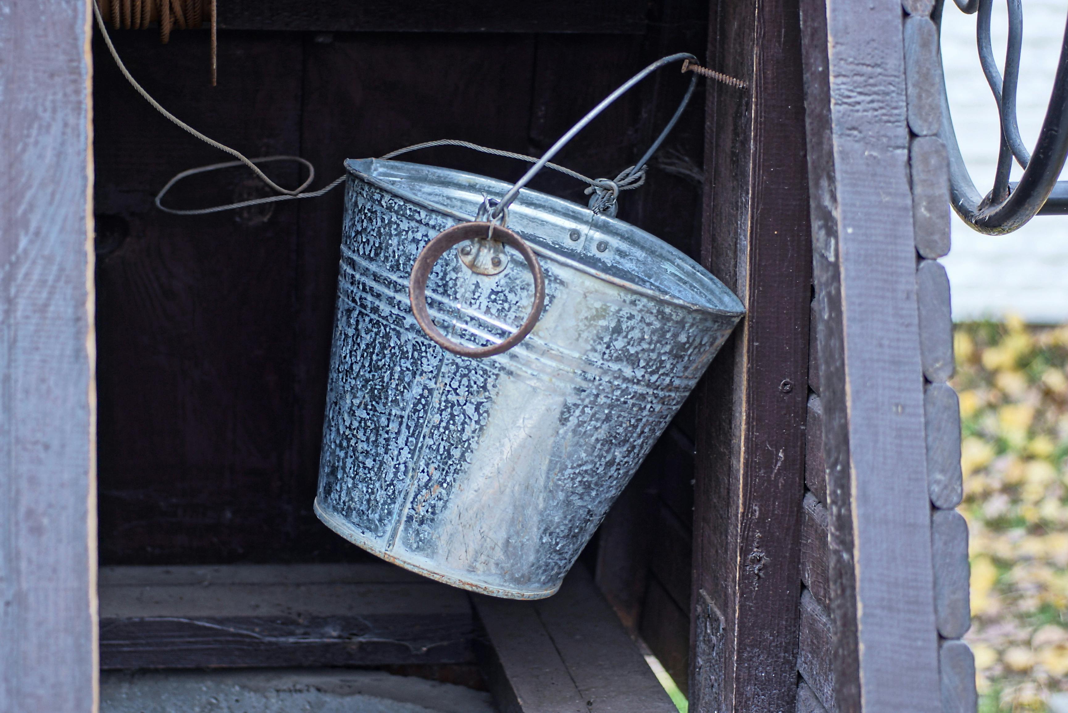 One gray metal bucket hangs on a brown wooden wall inside an old rural well outside