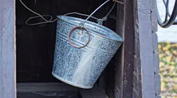 One gray metal bucket hangs on a brown wooden wall inside an old rural well outside One gray metal bucket hangs on a brown wooden wall inside an old rural well outside
