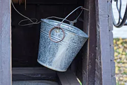 One gray metal bucket hangs on a brown wooden wall inside an old rural well outside One gray metal bucket hangs on a brown wooden wall inside an old rural well outside