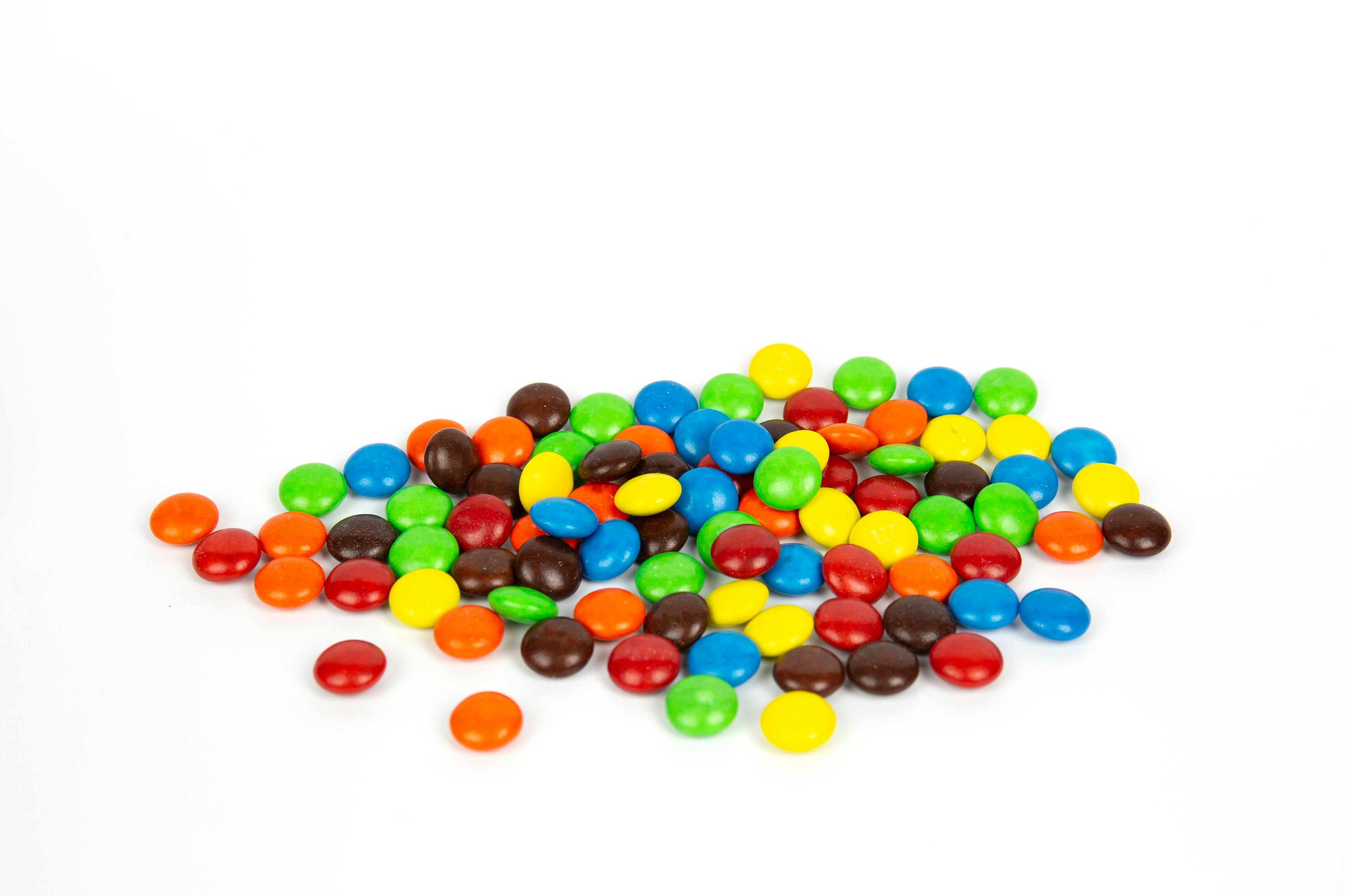 Colorful chocolate M&Ms in and out of focus on white background.