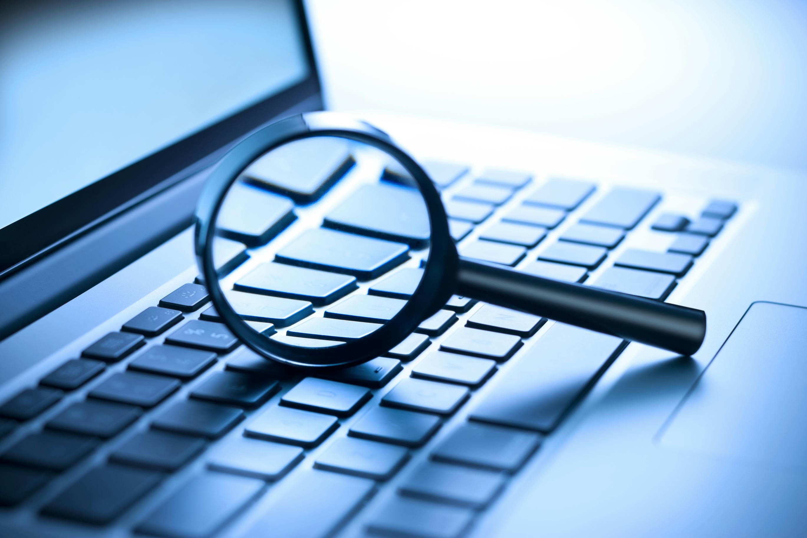 A laptop computer with a magnifying glass on the keyboard.