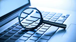 A laptop computer with a magnifying glass on the keyboard.