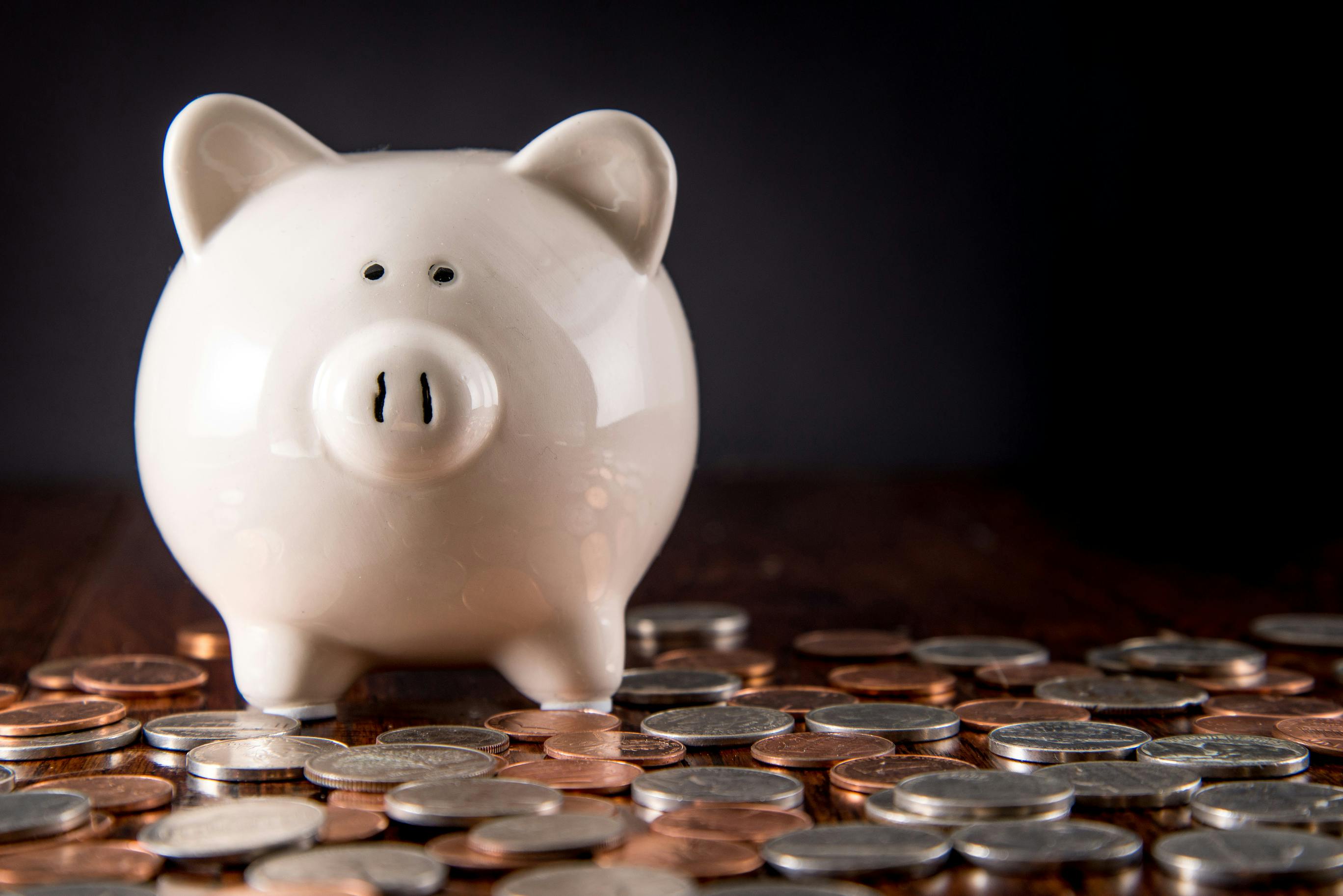 Piggy Bank on dark Hardwood Floor surrounded by scattered coins / USD money with a black background