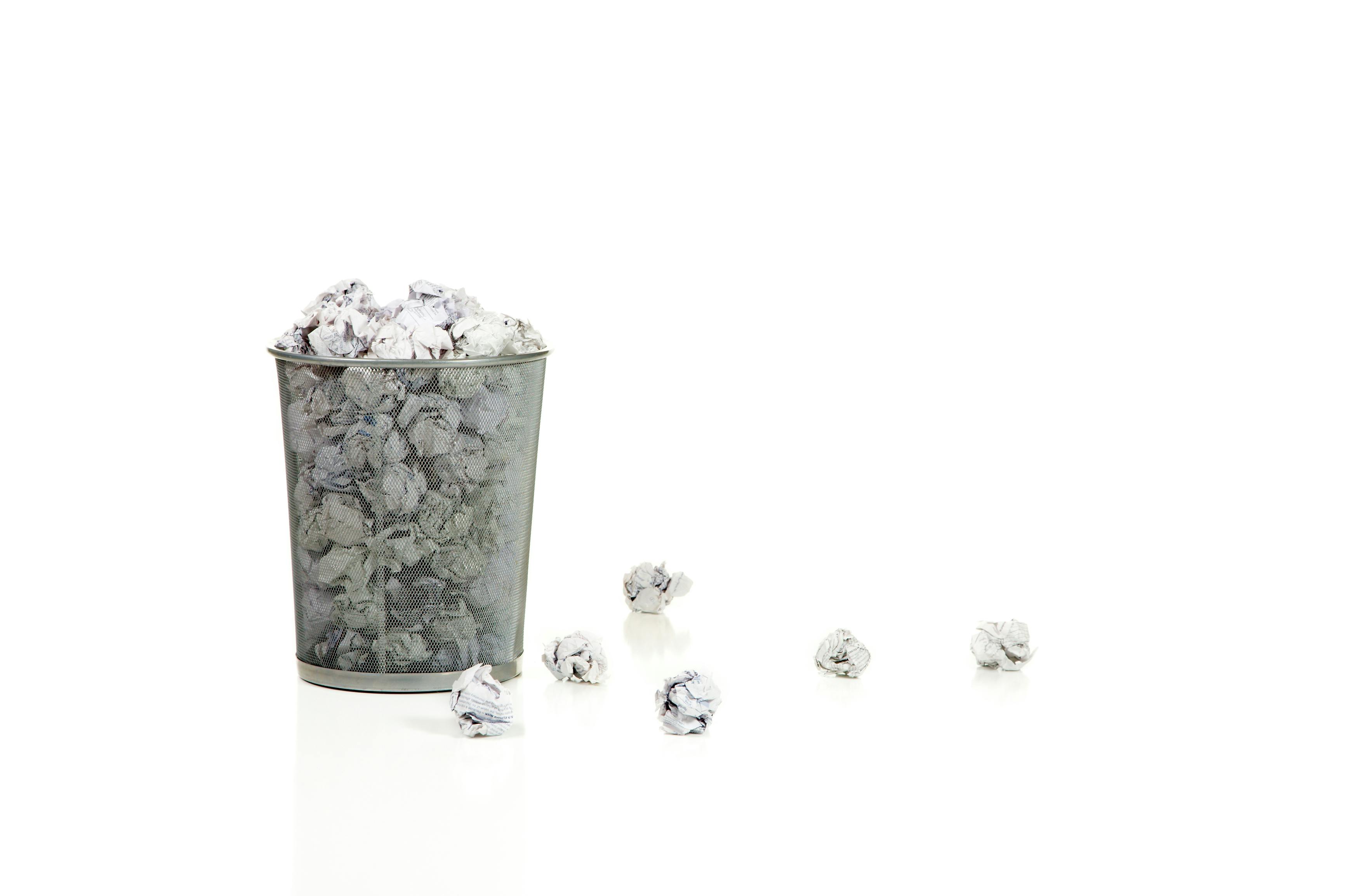 Metal mesh waste basket overflowing with paper balls isolated on white