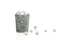 Metal mesh waste basket overflowing with paper balls isolated on white