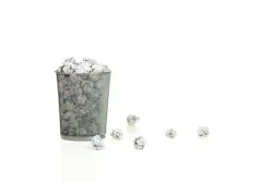 Metal mesh waste basket overflowing with paper balls isolated on white