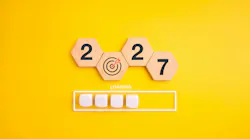 Wooden hexagon blocks form 2027 with bullseye replacing zero above loading bar on a yellow background. Preparation, progress tracking, strategic goals and readiness for the new year concept