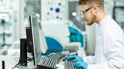A man in a lab coat works in a computer in a healthcare lab setting. A man in a lab coat works in a computer in a healthcare lab setting.