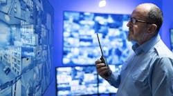 Photo of a man looking at a wall of computer screens, with a blue background. Photo of a man looking at a wall of computer screens, with a blue background.