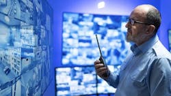Photo of a man looking at a wall of computer screens, with a blue background. Photo of a man looking at a wall of computer screens, with a blue background.