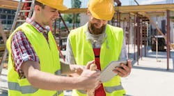 Two male workers in safety vests collaborating outside. Two male workers in safety vests collaborating outside.