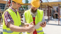 Two male workers in safety vests collaborating outside. Two male workers in safety vests collaborating outside.