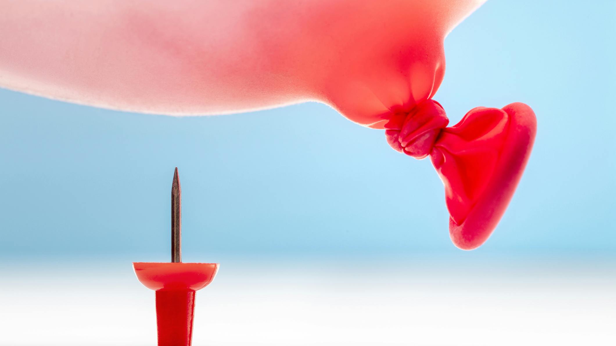 Thumbtack under a red balloon about to pop it.