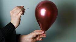 Woman’s hand holding a needle close to the side of a maroon-colored balloon to pop it. Woman’s hand holding a needle close to the side of a maroon-colored balloon to pop it.