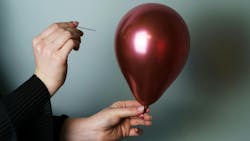 Woman’s hand holding a needle close to the side of a maroon-colored balloon to pop it. Woman’s hand holding a needle close to the side of a maroon-colored balloon to pop it.