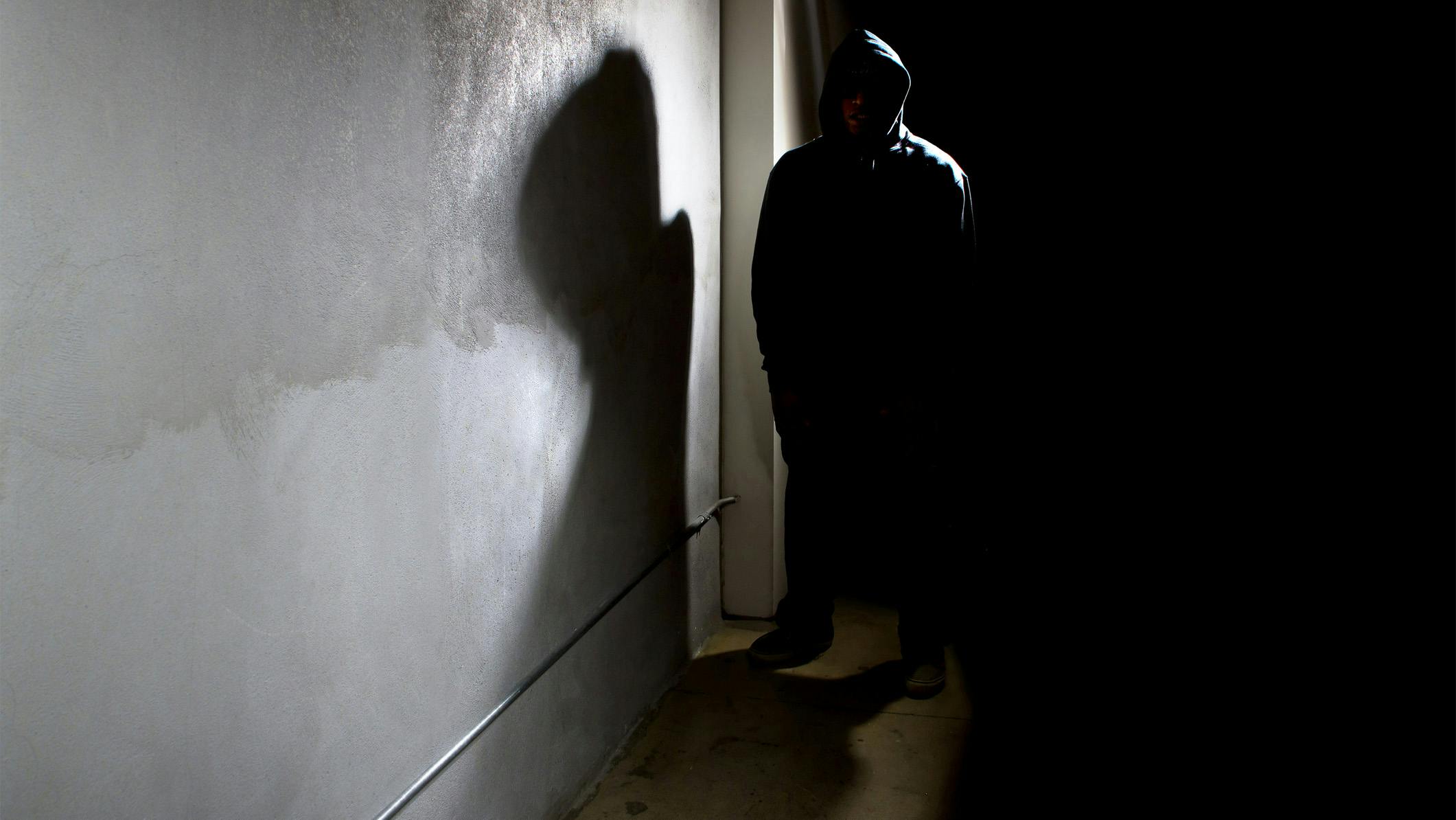Silhouette of scary hooded criminal in the shadows.