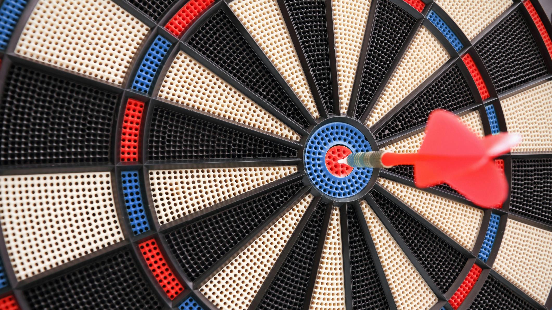 Red dart hitting the bullseye on a dart board.