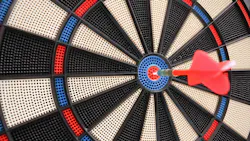 Red dart hitting the bullseye on a dart board.