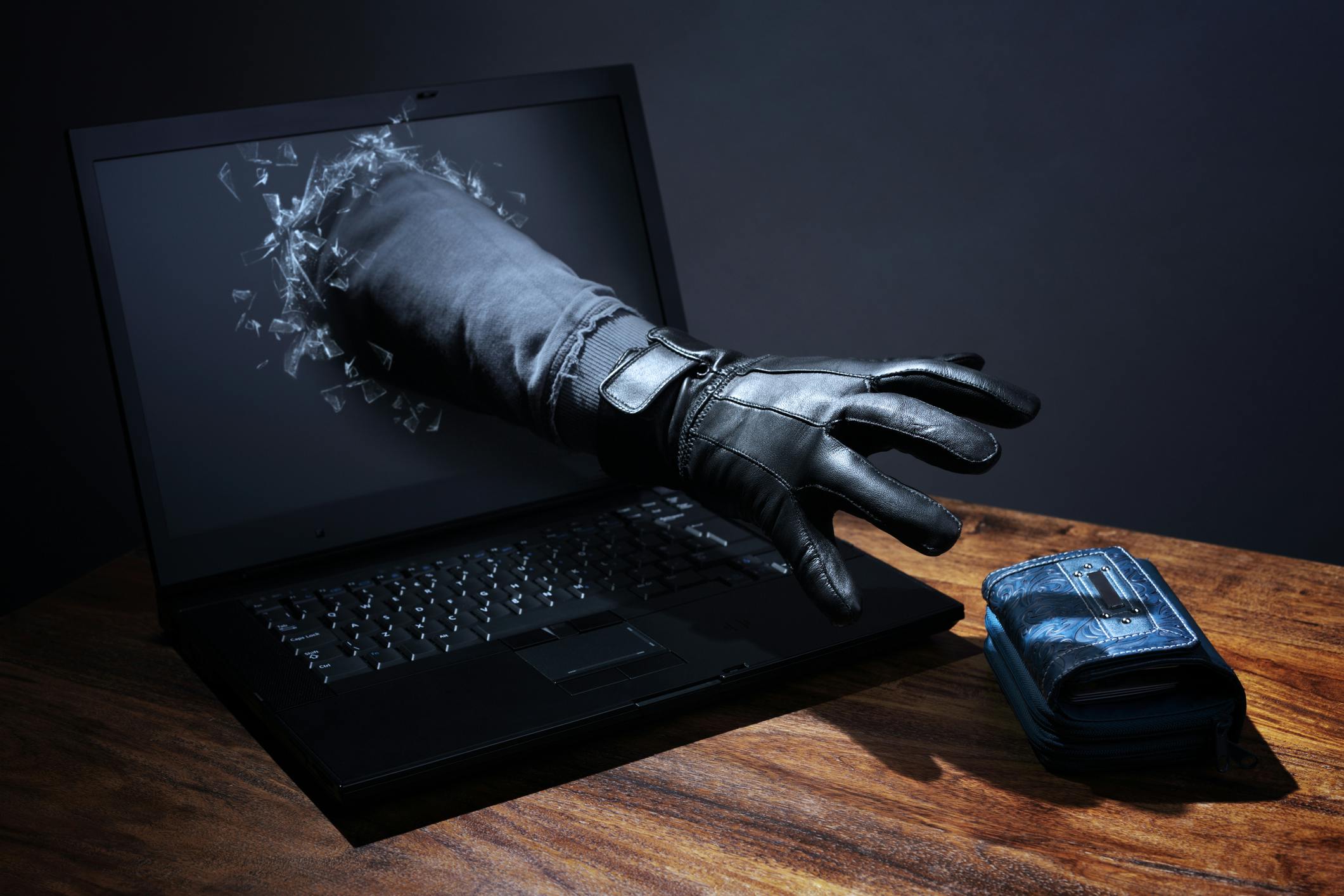 Concept of network hacker reaching arm through a laptop to steal a purse.