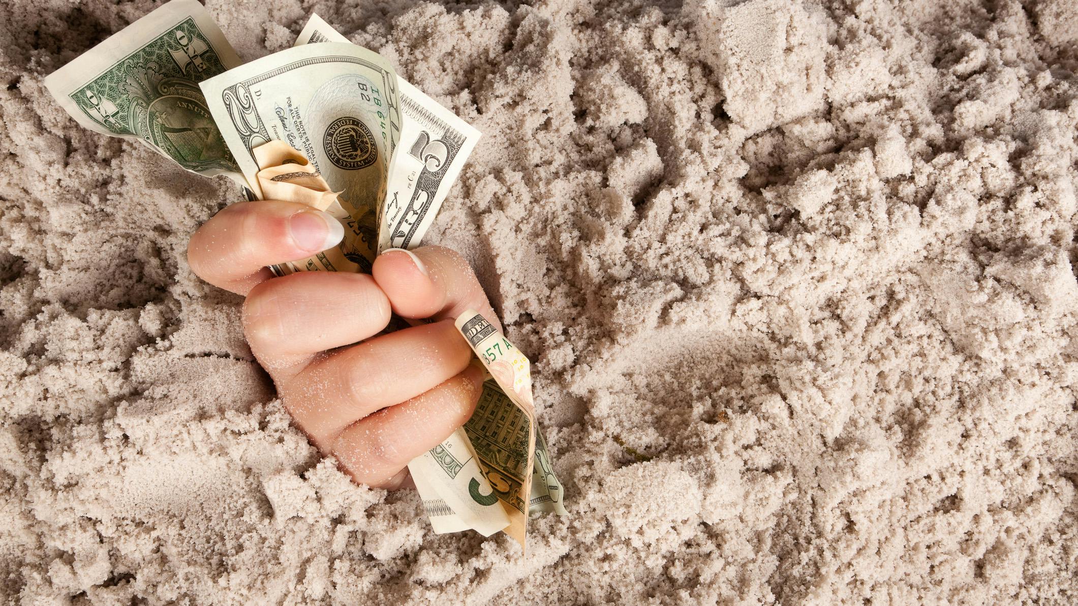 Female hand drowning in quicksand holding money.
