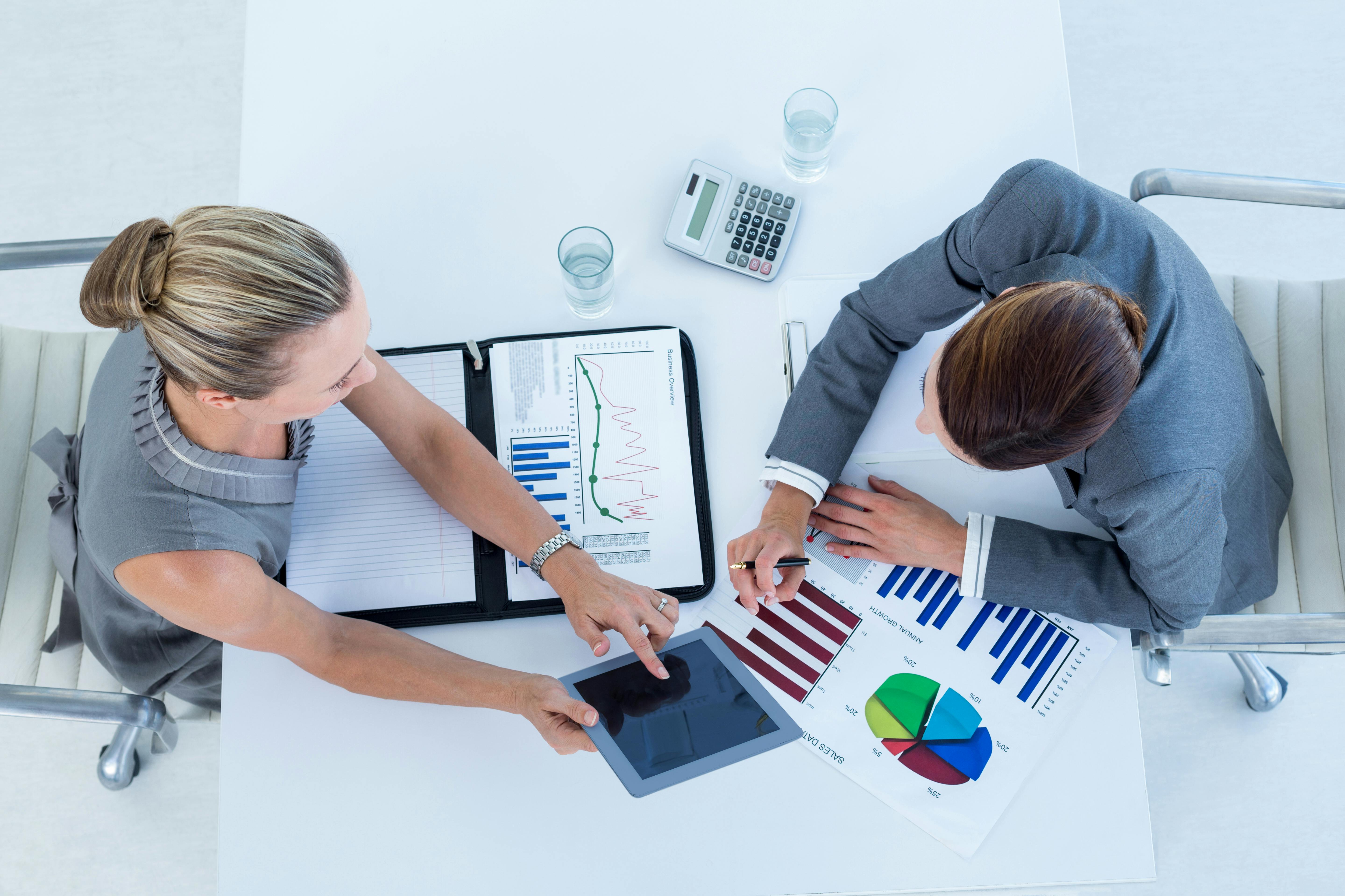 Business man and woman collaborating using financial documents and iPad.