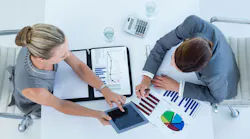 Business man and woman collaborating using financial documents and iPad.