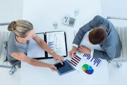 Business man and woman collaborating using financial documents and iPad.
