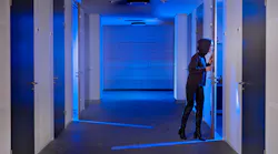 Concept of computer hacking with human in black hoodie sneaking through a door standing ajar in a dimly lit hallway.