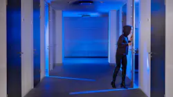 Concept of computer hacking with human in black hoodie sneaking through a door standing ajar in a dimly lit hallway.